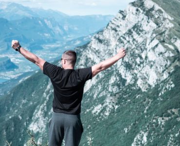 Man standing with arms raised in celebration overlooking a breathtaking mountain landscape.