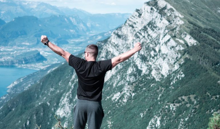 Man standing with arms raised in celebration overlooking a breathtaking mountain landscape.